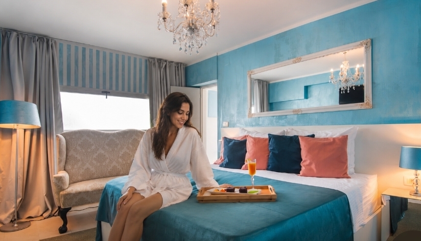A guest in a robe with breakfast on a tray in a blue villa bedroom